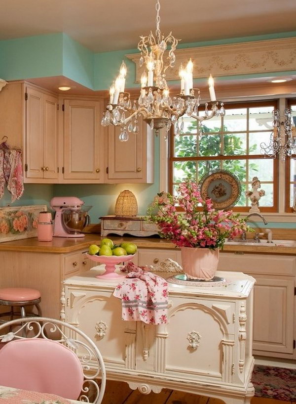Shabby Chic look. This gorgeous vintage white French island adds to elegant and chic feelings to this cream and pastel color themed kitchen. It is really fitting everything, the lovely ornate elements painted over in a soft cream, a chandelier hangs from the ceiling, and retro kitchen aid appliances in pink enamel and so on. 
