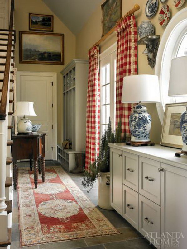 Farmhouse mud room. Classic blue and white relics ecco other traditional decors like an Oushak rug, mahogany buffet and red and white check curtains.  And the open storage area features hunting gear belonging to the designer’s family and friends. 